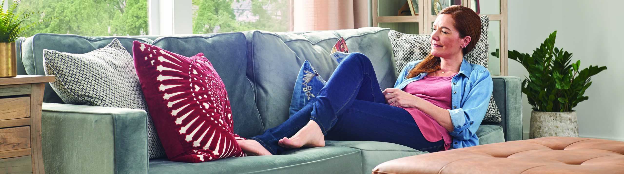 Woman reading magazine while relaxing on couch.