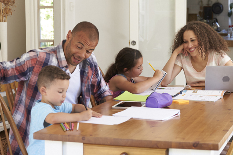 Parents Helping Children With Homework At Table.